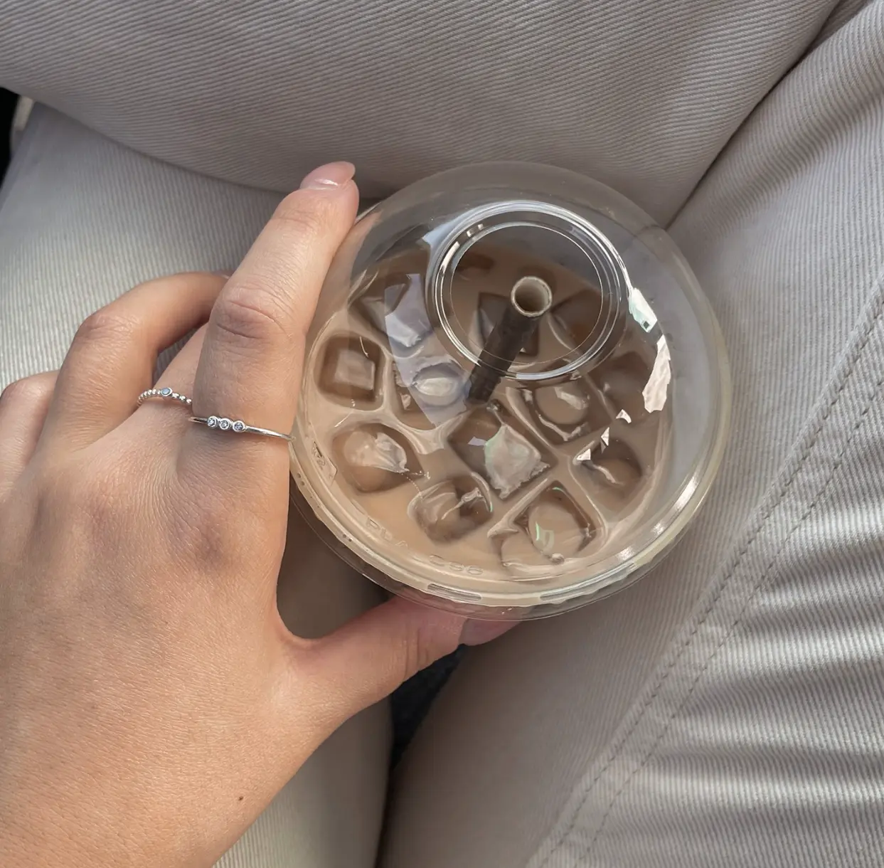 Hand wearing silver rings holding iced coffee